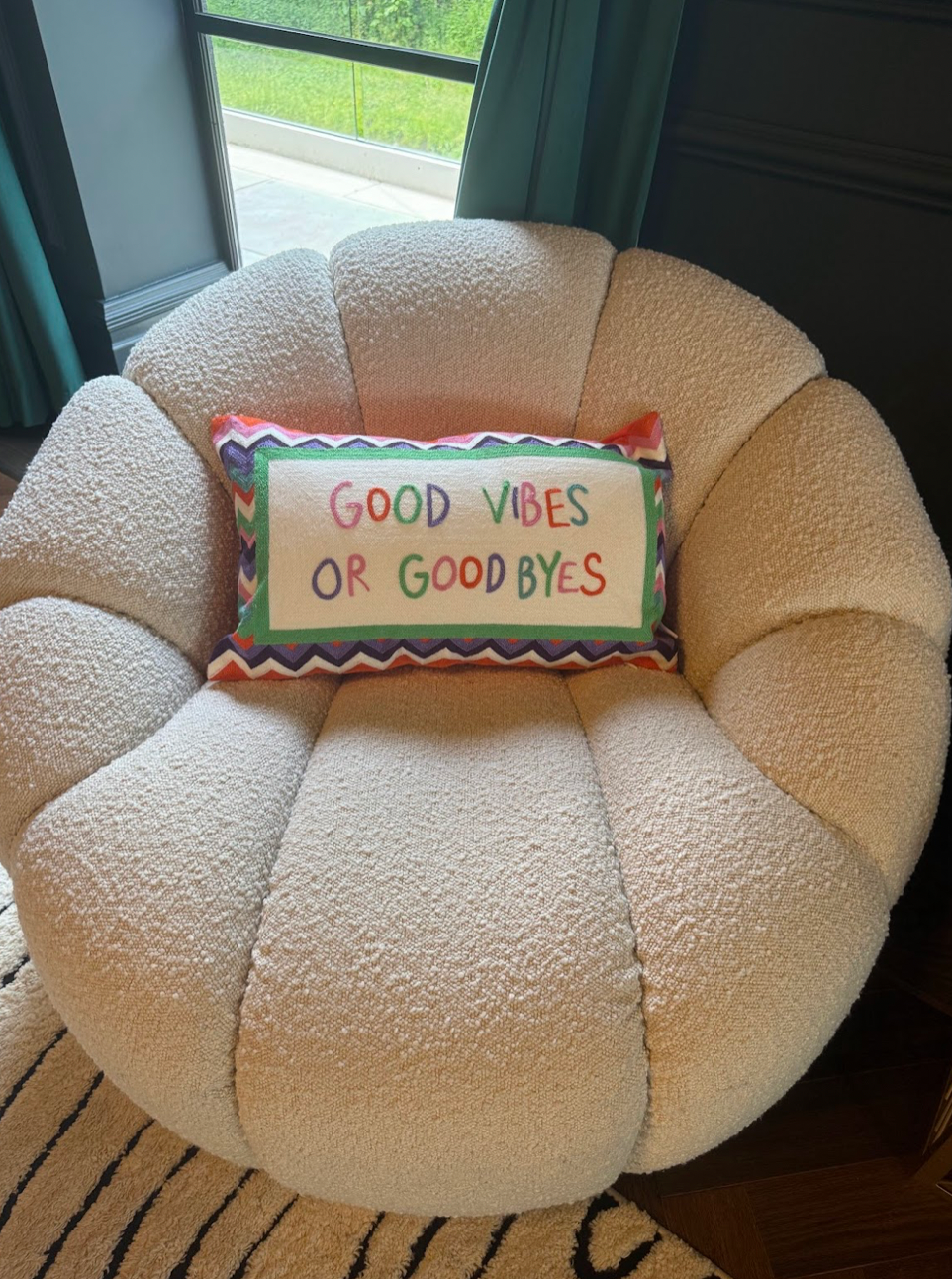 Round beige cushion with a colorful pillow reading 'Good Vibes or Good Byes' on a chair.
